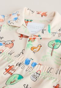 Dětská krémově zbarvená sada pyžama s ilustracemi farmových zvířat a přírody, včetně kachny, ovce, stromů, mrkví a lahve s mlékem.