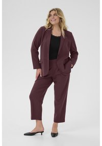 Veste bordeaux et pantalon fuselé assorti. La veste a des revers et des poches avant. Portée sur un haut noir avec une finition en dentelle.