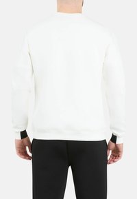 Sudadera blanca con cuello redondo y puños acanalados, que presenta un diseño sencillo y una textura suave, combinada con pantalones ajustados negros.