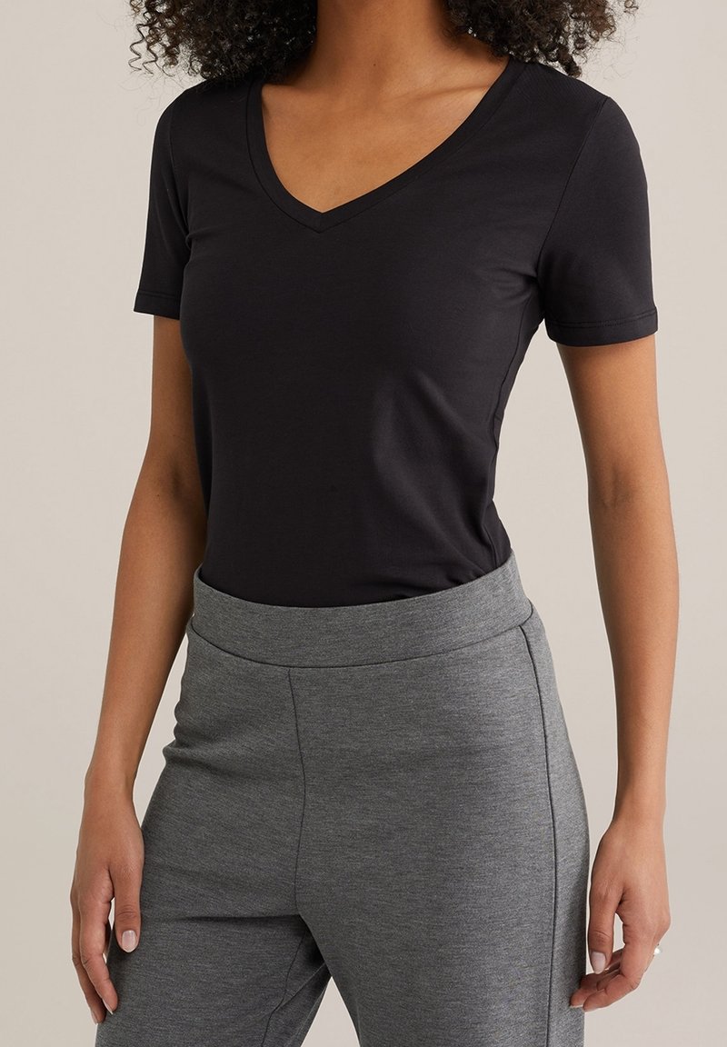 Czarna koszulka z krótkim rękawem i dekoltem w serek wykonana z miękkiego materiału, zestawiona z szarymi spodniami z wysokim stanem o gładkiej fakturze i elastycznym paskiem w talii.