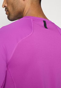 T-shirt de sport à manches longues en rose vif. Fabrication en tissu respirant avec des sections texturées et un accent noir au niveau de l'encolure arrière.