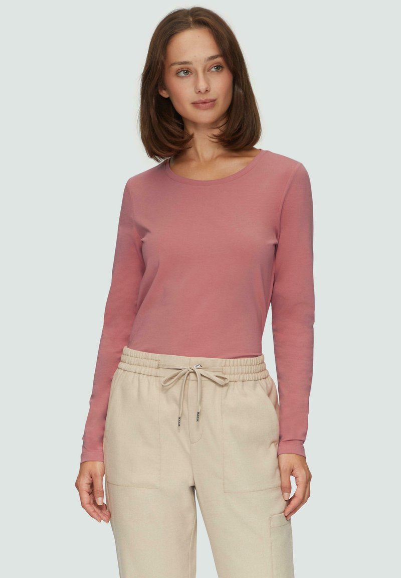 Langärmliges Oberteil mit Rundhalsausschnitt aus weichem, pinkfarbenem Stoff, kombiniert mit beigen, mit Kordelzug versehenen Hosen, die über gestickte Taschen verfügen. Sanfte Textur, taillierte Passform.