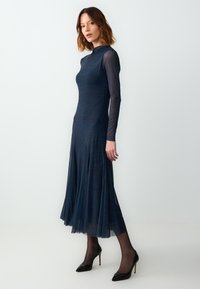 Abito lungo a maniche, di colore blu navy, con un corpino aderente e una gonna svasata, caratterizzato da un delicato motivo testurizzato, tessuti sovrapposti e maniche trasparenti.