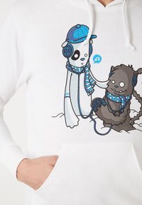 La sudadera blanca presenta un gráfico de un panda y un oso, ambos con auriculares y bufandas, con acentos azules y un detalle de nota musical.