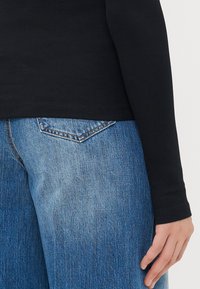 Black ribbed long-sleeve top paired with faded blue, wide-leg denim jeans featuring a back pocket with a diamond shape.