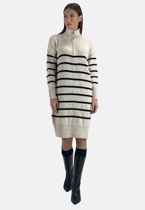 Robe pull en crème avec des rayures horizontales noires, col montant et poignets côtelés. Associée à des bottes noires montantes.
