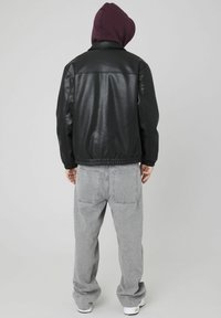 Veste en cuir noir avec des poignets et un ourlet élastiques, portée sur un sweat à capuche bordeaux. Assortie à un pantalon en denim ample gris clair.
