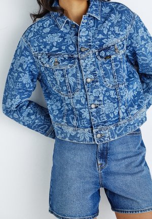 Denim jacket with floral and text print, buttoned front, chest pockets, paired with plain denim shorts.