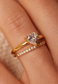 Goldfarbener Ring-Satz mit einem herzförmigen, klaren Edelstein und einem zweiten Band, das mit kleinen, runden klaren Kristallen verziert ist.