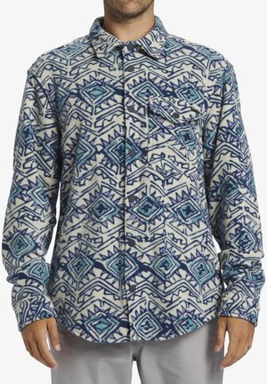 Fleece shirt with a geometric pattern in blue, purple, and cream. Features a button-up front and a single chest pocket. Long sleeves.