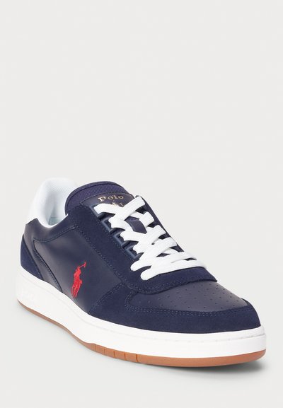 Navy blue sneaker with leather and suede materials, white laces, perforated toe, gum rubber outsole, and red logo accent on the side.