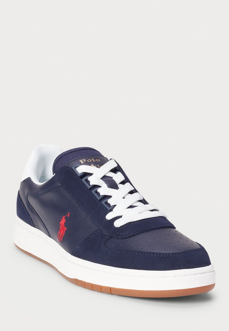 Baskets bleu marine en cuir et suède, avec lacets blancs, bouton perforé, semelle en caoutchouc gomme, et accent logo rouge sur le côté.