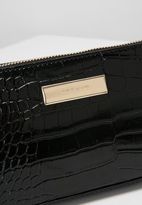 Pochette noire à texture crocodile avec fermeture éclair dorée et plaque métallique rectangulaire dorée gravée du logo River Island.