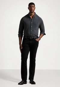 Pilkas marškinėliais su ilgomis rankovėmis, juodos lieknos kelnės ir juodi batai. Marškinėliai turi subtilią tekstūrą ir klasikinį apykaklę.