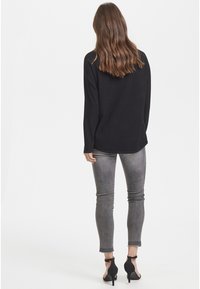 Schwarzes Langarmoberteil, kombiniert mit grauen Skinny Jeans. Schwarze Pumps mit Knöchelriemen. Glattes Material, lässiger Schnitt und schlichtes Design.