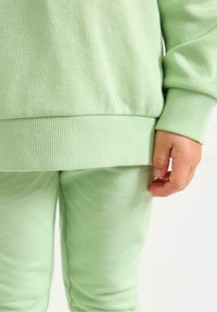 Helles grünes Sweatshirt und passende Hose aus weichem Stoff. Besitzt gerippte Bündchen und einen elastischen Bund für eine enge Passform.