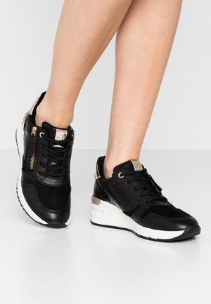Baskets de sport noires avec un mélange de cuir lisse et texturé, accents dorés, et une fermeture éclair sur le côté, présentant une semelle intermédiaire blanche et une semelle extérieure noire.