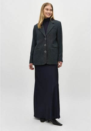 Charcoal herringbone blazer with two buttons and flap pockets, paired with a long navy skirt. Textured fabric, fitted silhouette.
