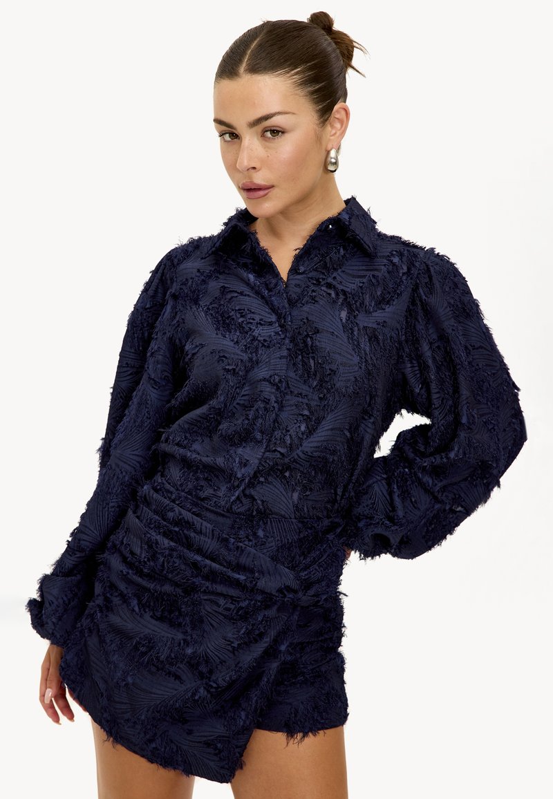 Navyblauw overhemd met gestructureerde, franjerijke stof. Voorzien van een puntige kraag en lange mouwen, met een getailleerd ontwerp aan de taille.