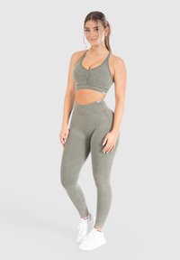 Olivgrön träningsset bestående av en kort, V-ringad topp med rynkningar, i kombination med högmidjade leggings, båda i mjukt, stretchigt tyg.