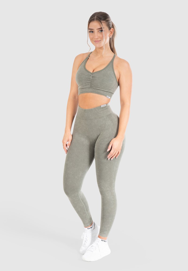 Olivgrön träningsset bestående av en kort, V-ringad topp med rynkningar, i kombination med högmidjade leggings, båda i mjukt, stretchigt tyg.