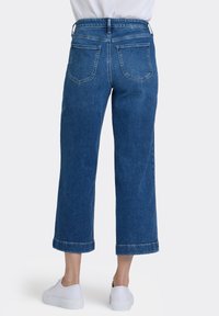 Blå denimjeans i culottestil med hög midja, uppvikta fållar och två bakfickor. Bärs med vita sneakers.