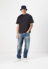 Black cotton t-shirt, relaxed fit, paired with light blue distressed jeans. White sneakers complete the look, accessorized with a black bucket hat.