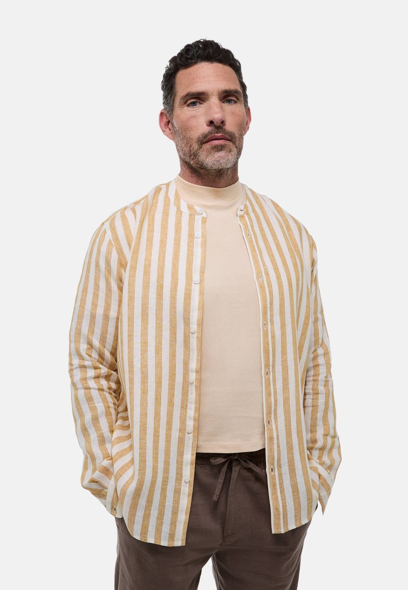 Chemise à rayures boutonnée en lin doux ; présente des rayures horizontales jaunes et blanches, une texture douce et un col rond. Portée par-dessus un haut beige.
