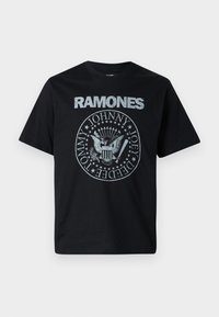 Melnas kokvilnas T-krekls ar grafisku druku, kurā redzams "RAMONES" baltiem burtiem un apļa dizains ar ērgļiem un vārdiem pelēkā krāsā.