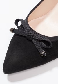Chaussure en daim noir à bout pointu, ornée d'un nœud en ruban noir décoratif et d'accents en métal argenté sur le bout. Doublure intérieure lisse.
