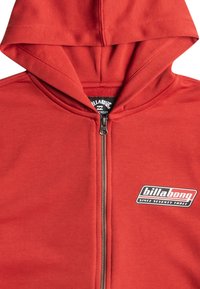 Röd zip-up hoodie i slätt tyg med en framsida dragkedja, med en svart och vit Billabong-logotyp på vänster bröst.