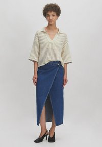 Brede crème gebreide top met een V-hals en korte mouwen, gecombineerd met een hooggeworlde donkerblauwe spijkerrok met wikkel ontwerp, voorzien van een zijsplit en knoopdetails.