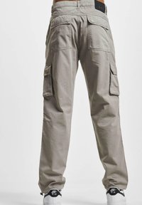 Beige cargo pants with a loose fit, multiple pockets, and a waistband label. Made from durable fabric, featuring a smooth texture.