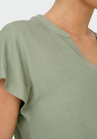 Ljusgrön linne-topp med V-ringning och korta ärmar, med en texturerad yta och en avslappnad passform.