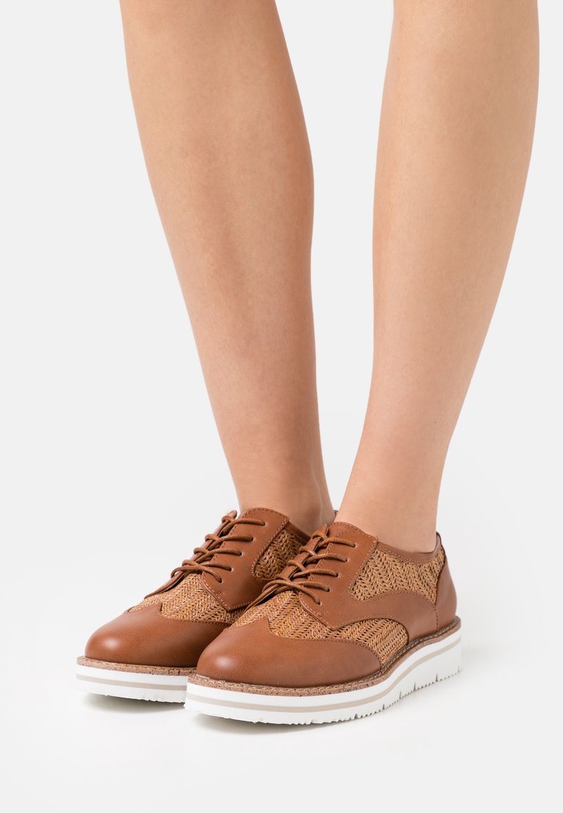 Chaussures en cuir marron à lacets avec une tige tissée, bout rond et semelle texturée blanche. Convient pour un usage décontracté ou semi-formel.