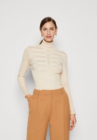 Hellebeige, gerippter Rollkragenpullover mit horizontalen Streifen; kombiniert mit hoch taillierten, weit geschnittenen, hellbraunen Hosen. Weiche Textur, figurbetontes Design.