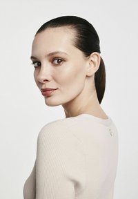 Jasno beżowy sweter z prążkowanej tkaniny, z okrągłym dekoltem, dopasowany krój oraz subtelny złoty akcent z tyłu. Gładka tekstura, minimalne zdobienia.