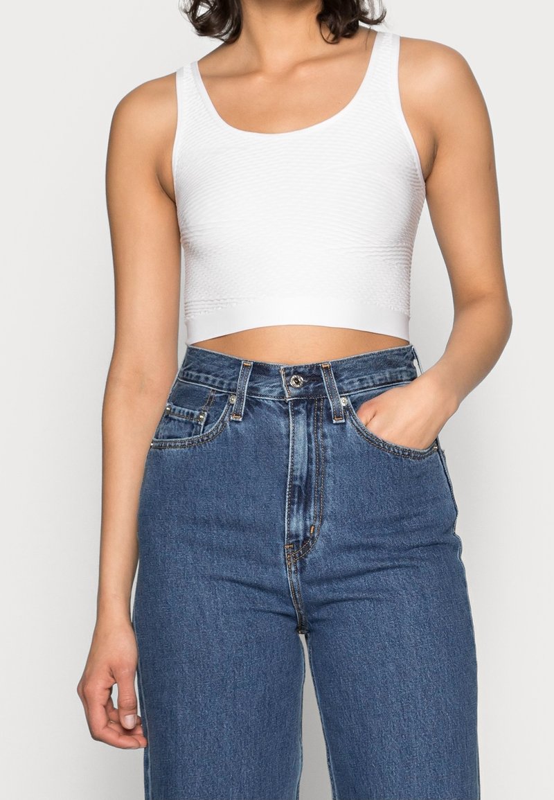 White ribbed crop tank top with wide straps, paired with high-waisted blue denim jeans featuring a button closure and front pockets.