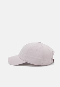 Gaiši rozā Nike beisbola cepure ar baltu swoosh logotipu, regulējama siksniņa un izšūtas aciņas uz balta fona.
