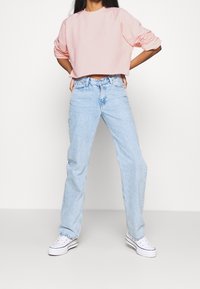 Felpa cropped rosa chiaro con scollo rotondo e maniche ampie, abbinata a jeans a gamba dritta azzurri e sneakers bianche.