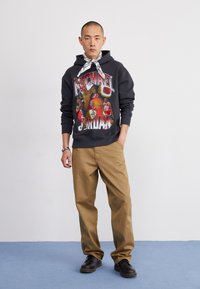 Felpa nera con stampa grafica a tema basket, abbinata a pantaloni beige e scarpe nere. Accessoriata con un bandana bianco.