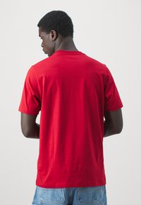 Red cotton t-shirt with short sleeves, classic crew neck. Smooth texture, no visible patterns or graphics, plain back view.