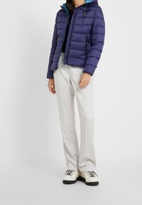 Giacca a piumino blu navy con cappuccio, design trapuntato e fodera a contrasto turchese. Abbinata a pantaloni larghi di colore chiaro e stivali bianchi.