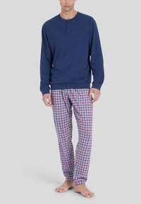 Maglietta henley a maniche lunghe blu navy con tre bottoni, abbinata a pantaloni da pigiama a quadri rossi, bianchi e blu con vita elastica.