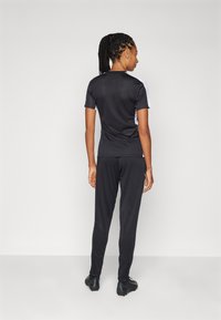 Zwart sportshirt en broek met een slim fit ontwerp, korte mouwen en contrasterende witte accenten. Zachte textuur en lichtgewicht stof.
