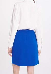 Bílé dlouhé rukávy košile s knoflíkovými manžetami, spárovaná s úzkou modrou sukní. Sukně má hladkou texturu a zadní šev.