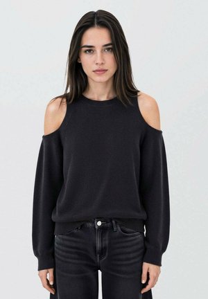 Pull en tricot noir avec un design à épaules dénudées, manches longues et texture en maille côtelée. Assorti à un jean foncé ajusté.