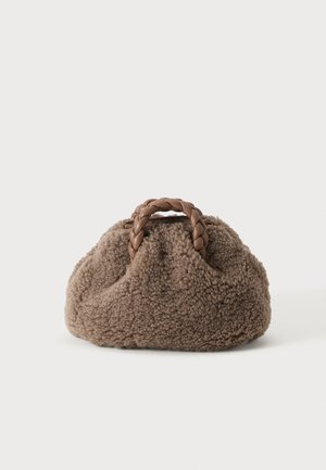 Kleine braune flauschige Handtasche mit geflochtenen Ledergriffen auf einfarbigem hellem Hintergrund.