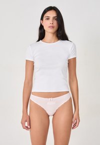 Camiseta blanca de manga corta combinada con braguitas de encaje rosa claro que presentan un pequeño lazo y detalle bordado en la parte frontal.