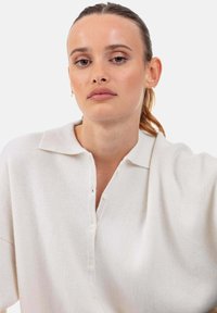 Weißer, kragenloser Strickpullover mit einer Knopfleiste, der einen lockeren Schnitt und eine weiche Textur aufweist. Schlichtes Design, ohne sichtbare Muster oder Akzente.